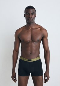 Sorte boxer briefs med en teksturert olivengrønn midjebånd som har et subtilt mønster og et svart logo-merke foran. Glatt stofffinish.