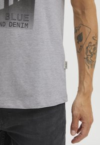 Grå bomull T-skjorte med rund hals, prydet med et svart grafisk trykk og en liten merkeetikett på kanten, kombinert med mørke jeans.
