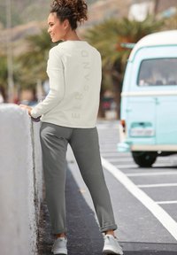 Helles cremefarbenes Sweatshirt mit dezentem "ELBSAND"-Druck; kombiniert mit grauen Jogginghosen. Weiße Sneakers runden den lässigen Look ab.