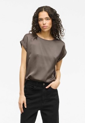Blusa a maniche corte di colore marrone scuro in un tessuto liscio e leggero, abbinata a jeans neri a vita alta. Entrambi i capi presentano una vestibilità comoda.