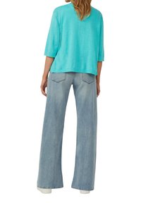 Maglione azzurro a maniche tre quarti, morbido e ampio, abbinato a jeans a gamba larga di un blu chiaro con una finitura sbiadita e tasche laterali.