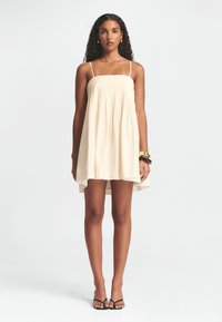 Heled kreemjas suvekleit õhukeste rihmadega, kokku kogutud rinnaosa ja voolava A-line kujuga. Omab kõrge-esise ja madalama tagaosa hemmi, samuti krõbedat tekstuuri.