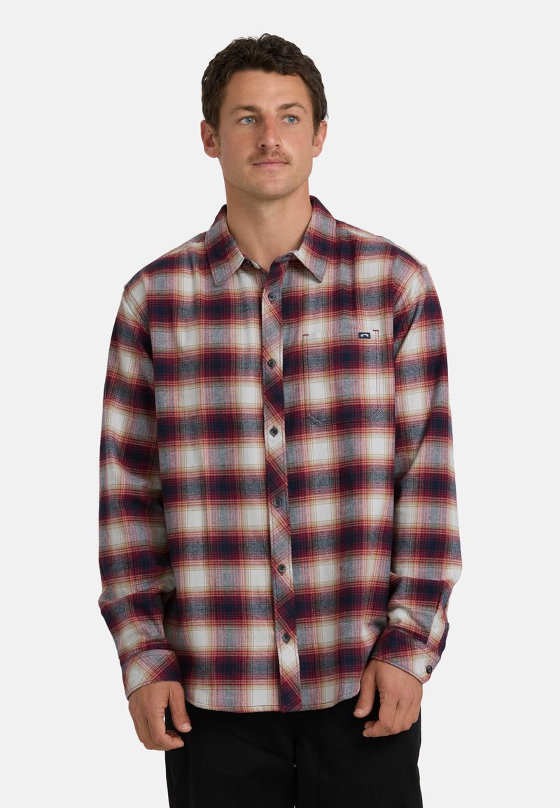 Camicia di flanella a quadri nei toni di rosso, bianco e blu; maniche lunghe con polsini a bottone e una tasca sul petto con un piccolo logo.