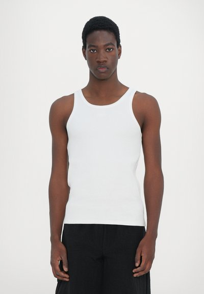 Weißes Baumwolltanktop mit einer taillierten Passform, breiten Schulterträgern und glatter Textur, kombiniert mit lockeren schwarzen Hosen.