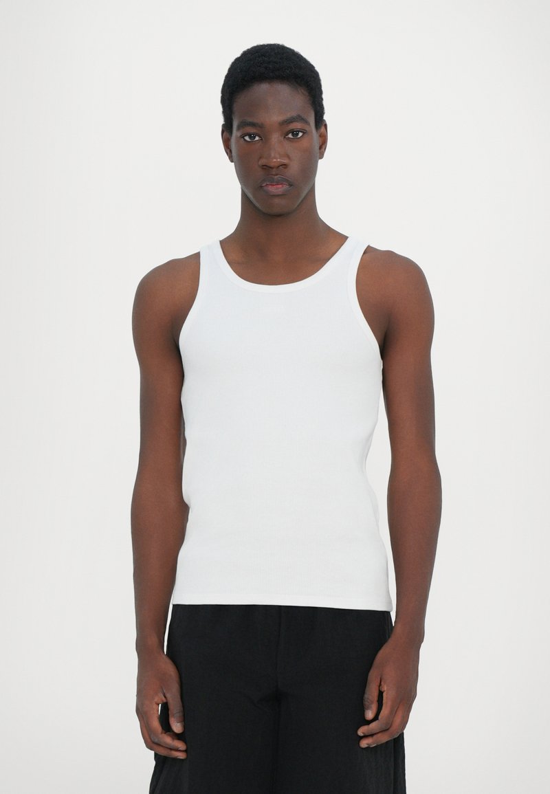 Débardeur en coton blanc à la coupe ajustée, avec de larges bretelles et une texture lisse, associé à un pantalon noir ample.