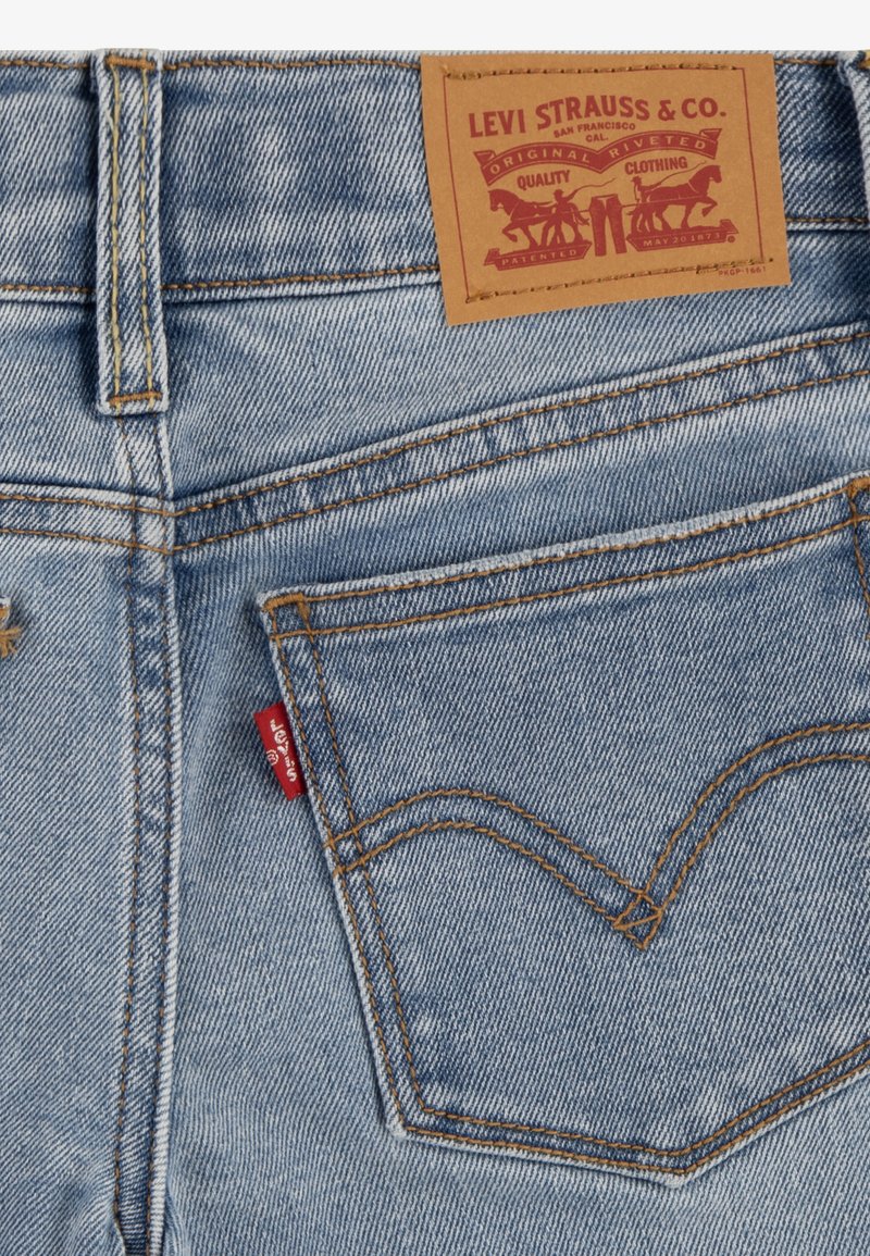 Hellblaue Denim-Jeans mit einem braunen Lederlabel. Zu den Merkmalen gehören orangefarbene Nähte und ein rotes Logotab auf der Gesäßtasche.