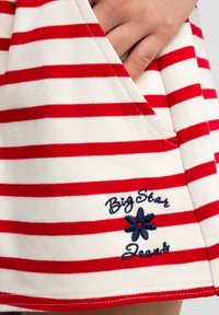 Raudonai ir baltai dryžuota sijonas su kišene ir siuvinėtu "Big Star Jeans" užrašu su mėlynos gėlės akcentu. Minkšta, medvilninė medžiaga.