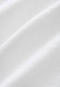 Primo piano di un morbido tessuto di cotone bianco con pieghe soffici e una sottile trama intrecciata.