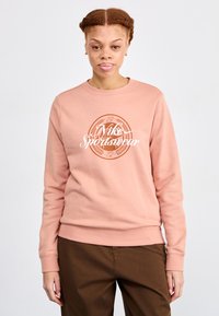 Lys rosa sweatshirts med en hvit "Nike Sportswear" logo og sirkulært design. Tøyet ser mykt ut med ribbede mansjetter og kant.