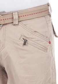 Beige Shorts aus Leinen mit einer strukturierten Oberfläche, ausgestattet mit einem gewebten Gürtel mit roter Naht und einer Reißverschlusstasche an der Seite.