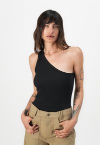 Body a costine nera con spalla scoperta, design aderente, abbinato a pantaloni khaki a vita alta, che mostrano una texture liscia e un profilo semplice.