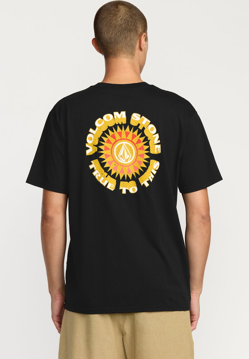 T-shirt noir à manches courtes avec un grand graphique jaune et rouge représentant un effet de rayon de soleil et le texte "VOLCOM STONE TRUE TO THIS" au dos.