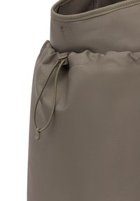 Close-up van een taupekleurige stoffen tas met een trekkoord en een plastic knopje om de opening aan te trekken.