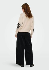 Beige knitted sweater with black abstract design on sleeves, paired with loose black corduroy pants, showcasing relaxed fit and texture.