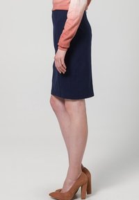 Jupe crayon marine au design ajusté, en tissu extensible, avec une ourlet subtil, portée avec des chaussures à talons hauts marron, mettant en valeur une silhouette élégante.