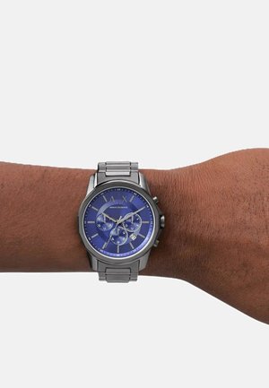 Silberner Edelstahl-Chronograph mit blauem Zifferblatt, silbernen Zeigern und Logo. Verfügt über strukturierte Glieder im Armband und ein Datumsfenster.