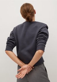 Tmavě šedá mikina s kulatým výstřihem a dlouhými rukávy. Tkanina se zdá být mírně texturovaná a střih je uvolněný.