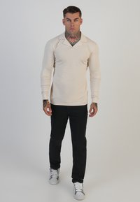 Beez pikikate varrukatega polo särk terava kraega, koos mustade pükste ja valgete tossudega. Kangas näeb sile ja hästi istuv.