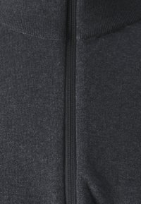 Mörkgrå dragkedjeplagg med texturerat tyg, utrustad med en kontrasterande svart dragkedja längs mitten, utan synliga mönster eller accenter.