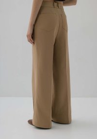 Szerokie, wysokie spodnie w beżowym kolorze o gładkiej fakturze. Posiadają dwie tylne kieszenie i detal paska w talii.
