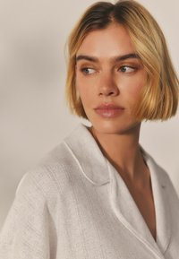 Lichtgrijze, gestructureerde shirt met een kraag, met subtiele horizontale patronen en een relaxte pasvorm. Model heeft kort blond haar.