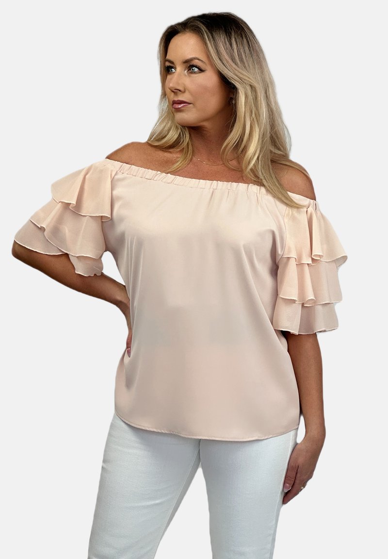Bluzka w kolorze bladoróżowym z odkrytymi ramionami, z warstwowymi falbanami na rękawach, gładką teksturą i luźnym krojem, w połączeniu z białymi spodniami.
