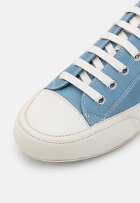 Zapatilla de cuero azul con punta de goma blanca, cordones blancos y costuras en contraste. Forma redondeada y detalle de superficie texturada.