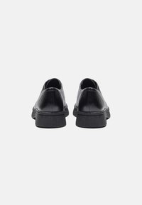 Black leather shoes with a textured finish, rounded toe, and low rubber soles. The back view highlights the smooth heel and subtle stitching.