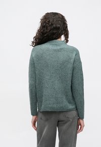 Groene geribbelde trui met een hoge hals, lange mouwen en een ontspannen pasvorm. De textuur lijkt zacht en gezellig, geschikt voor casual kleding.
