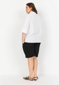 White collared shirt with three-quarter sleeves, paired with black shorts. Black sandals feature silver studs. Minimalist design and neutral colors.