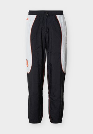 Black and white track pants with orange piping, elastic waistband, and a small orange logo on the left thigh.