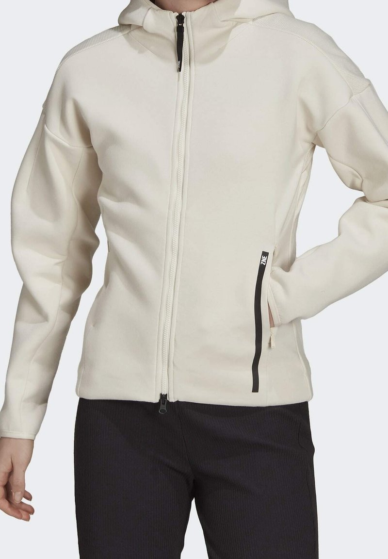 Světlobéžová mikina na zip s texturovaným povrchem, kapucí a černým zipem. Obsahuje boční kapsy s černými detaily. Hladký textilní povrch.