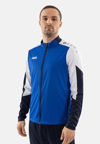 Blauwe en witte sportjack met een ritssluiting aan de voorkant, heeft een hoge kraag, zijzakken en een merklogo op de borst. Zachte stof met lange mouwen.