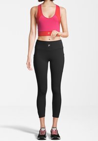 Fuksjowy stanik sportowy z okrągłym dekoltem i szerokimi ramiączkami, w zestawie z czarnymi legginsami o wysokim stanie z bocznymi kieszeniami. Czarno-różowe sneakersy.