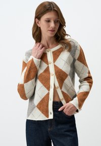 Cardigan en tricot à motif en losanges, présentant des couleurs orange, crème et gris. Il a un col rond et des boutons dorés. Tissu texturé.