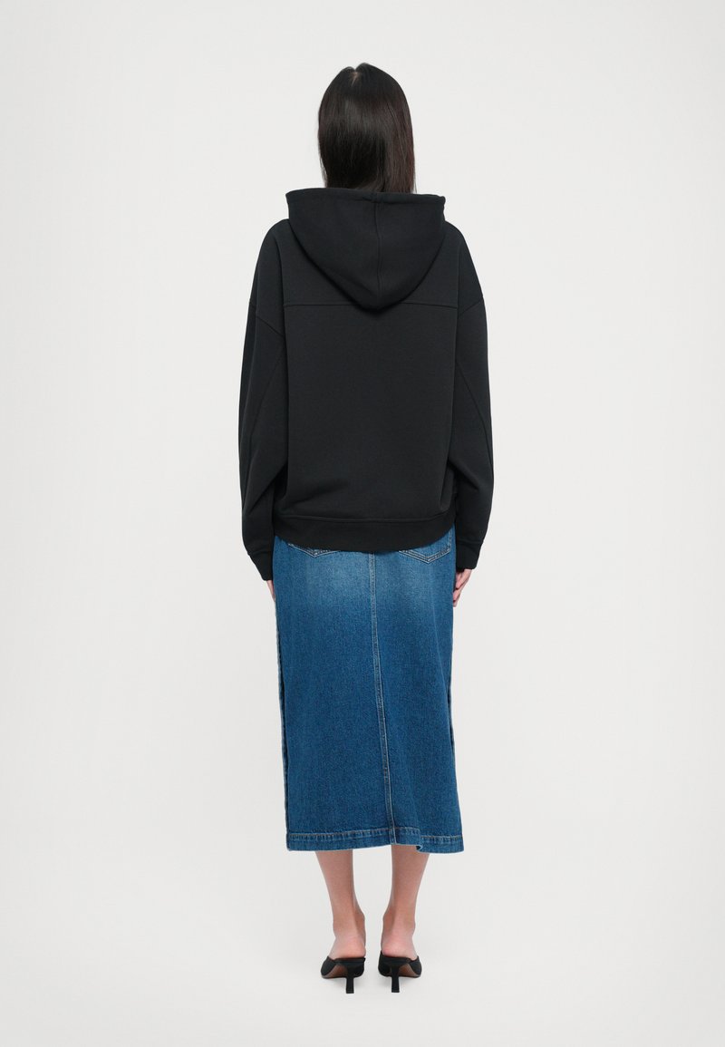 Sweatshirt à capuche noir, coupe oversize, associé à une jupe en denim bleu de mi-longueur. Texture lisse, avec un design simple et des fentes sur les côtés.