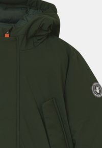 Grüne, wasserdichte Jacke mit Kapuze, mit einem Reißverschluss vorne, Seitentasche und einem Aufnäher am Ärmel. Glattes Material mit matter Oberfläche.