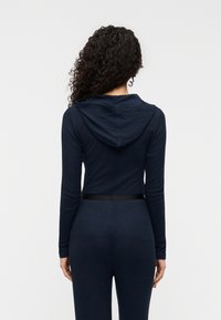 Μπλε σκούρο ολόσωμο φορμάκι με μακριά μανίκια, ριμπ υφή και εφαρμοστή μέση. Διαθέτει μαύρη ζώνη στη μέση και απαλό κουκούλι.