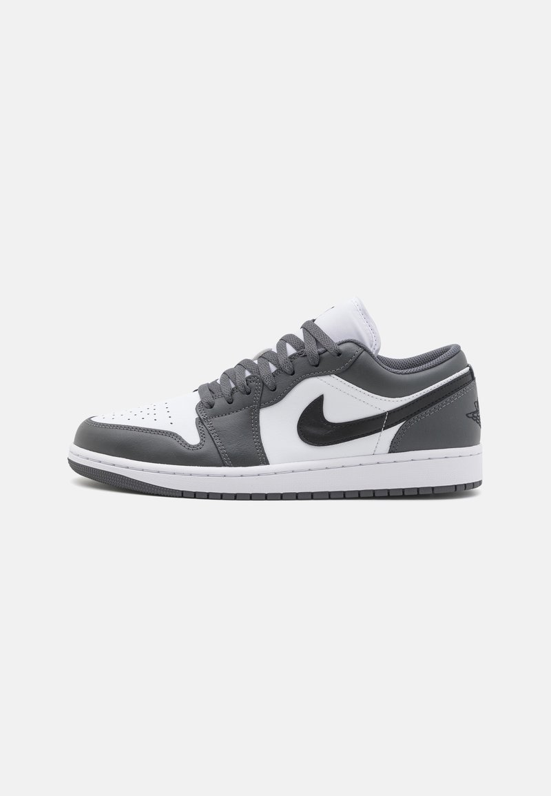 Basket basse avec des panneaux en cuir blanc et gris foncé, logo Nike swoosh noir, et lacets gris sur une semelle blanche sur fond uni.