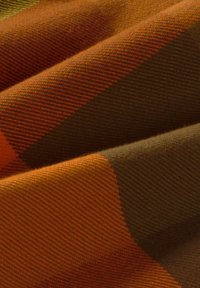 Textilie s jakardovým vzorem, která zobrazuje oranžové a hnědé kontrastní geometrické tvary, vykazující hladkou texturu a tkaný povrch.