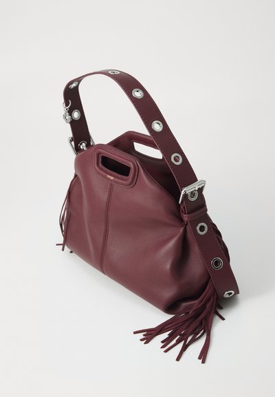 Burgundy nahkahandbag, jossa on rakenteellinen muoto, tupsu-yksityiskohdat ja koristeellinen hihna, jossa on hopeiset osat ja rei'itykset.