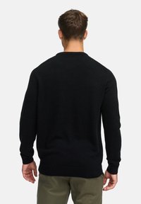Pull en tricot noir avec un col rond, présentant un ourlet et des poignets côtelés, vu de dos, avec une texture lisse et des détails minimes.