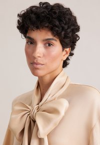 Blusa beige in seta, con un grande fiocco al colletto e una texture liscia, con una leggera lucentezza e un design minimalista.