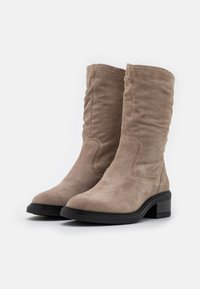 Suède laarzen tot de knie in taupe met een lichtjes versleten ontwerp, zwarte rubberen zool en contrasterende stikseldetails.