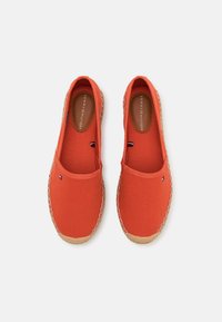 Raudonos drobės espadrilės su pintos jutos viršeliu. Šone yra mažas mėlynas, baltas ir raudonas logotipas. Lygi tekstūra, lengvai užsidedančios.