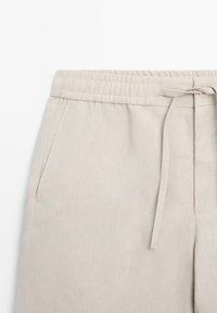 Light beige linen pants with elastic waistband, side pockets, and a front tie belt on a white background.