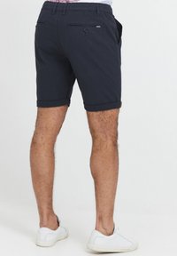 Pantaloni corti blu navy realizzati in tessuto leggero, con un taglio sartoriale, risvolti e due tasche posteriori con bottoni. Abbinate a sneaker bianche.