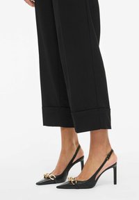 Črni usnjeni slingback čevlji z ostrim sprednjim delom, zlatim verižnim detajlom na sprednji strani in elegantnim visokim stiletto peto. Gladek tekstura.