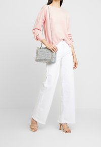 Jasnoróżowy sweter, białe szerokie spodnie i nagie sandały na obcasie. Błyszcząca pleciona torebka z łańcuszkiem, z niebieskimi i srebrnymi akcentami.