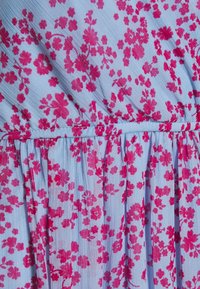 Vaaleansininen kangas, jossa on vaaleanpunaisia kukkakuoseja. Kootut vyötäröön liittyvät yksityiskohdat pehmeillä laskoksilla, jotka tekevät siitä ilmavan ja virtaavan.